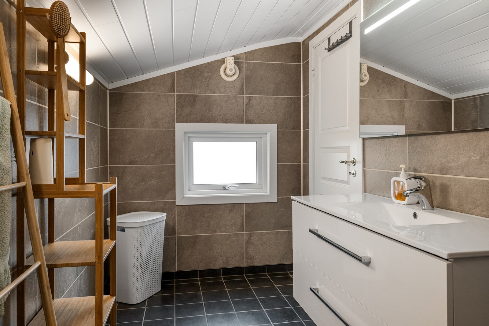 Badet har servant med underskap, speil over vask med innfelt lys . Galleribilde