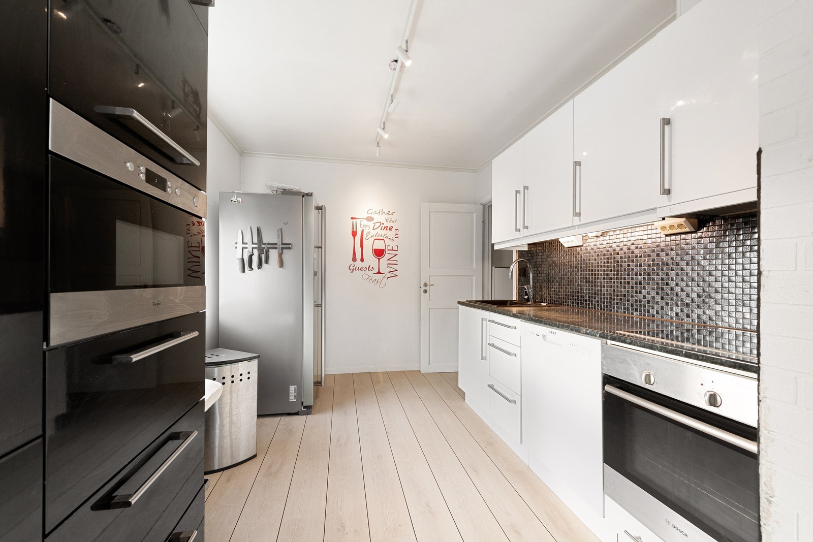 Kjøkken i hovedetasjen med hvite og sorte fronter. Integrerte hvitevarer samt frittstående kjøleskap Galleribilde