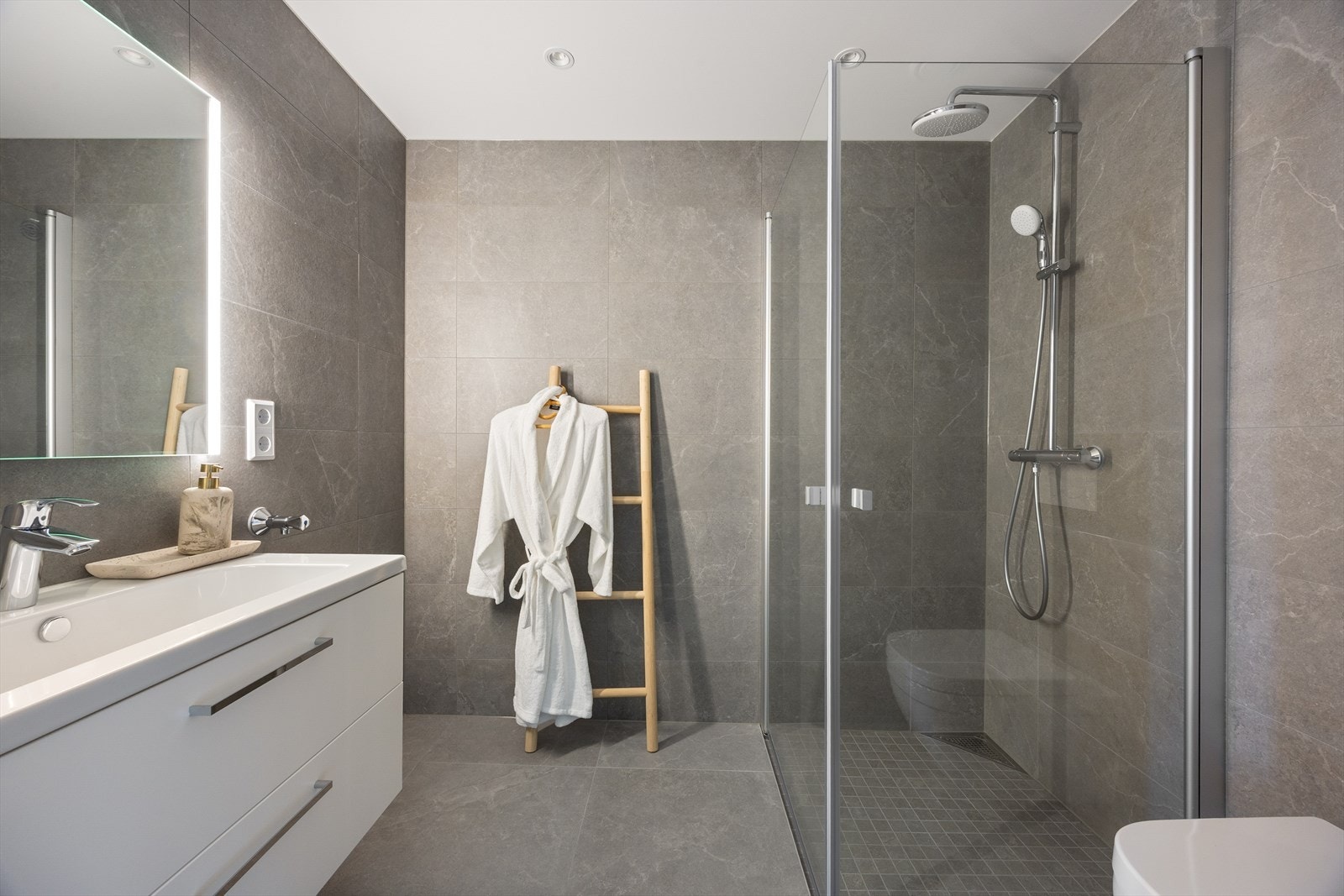 Delikat, flislagt baderom med varme i gulvet. Baderommet har innredning med nedfelt servant, veggmontert toalett, dusjvegger/hjørne og opplegg for vaskemaskin. Det er balansert ventilasjon. Galleribilde