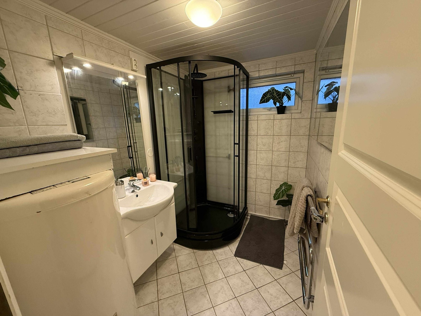 Dusjrom med fliser på gulv og vegger, servant med underskap, varmtvannsbereder og dusjkabinett. Rommet har vindu som gir naturlig lys og lufting, samt håndkletørker for økt komfort. Galleribilde