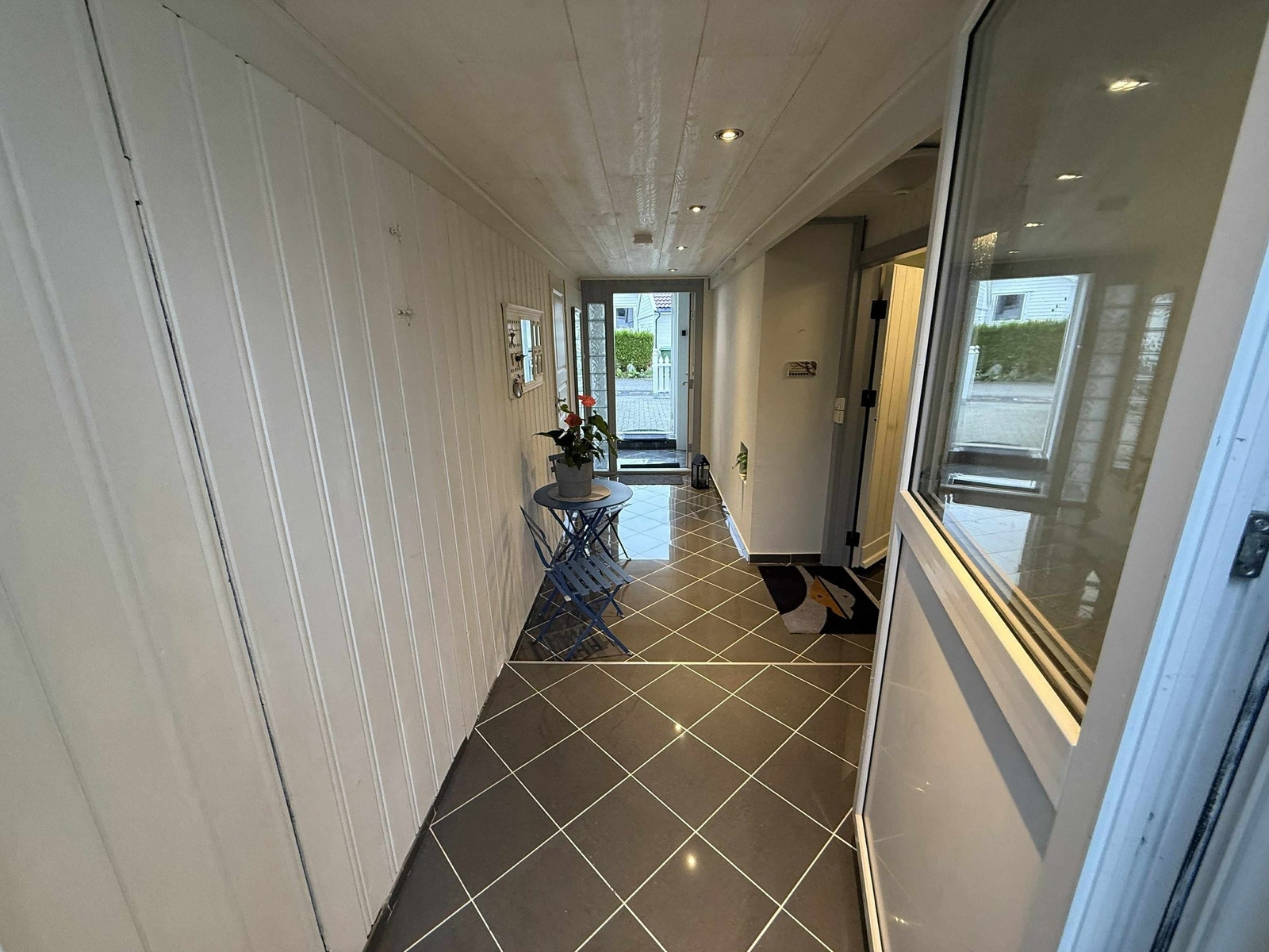 Boligen har en praktisk og gjennomgående gang med inngang fra både gårdsplass/ytterdør og direkte utgang til hagen på motsatt side. Gulvet er flislagt og enkelt å holde rent. Galleribilde