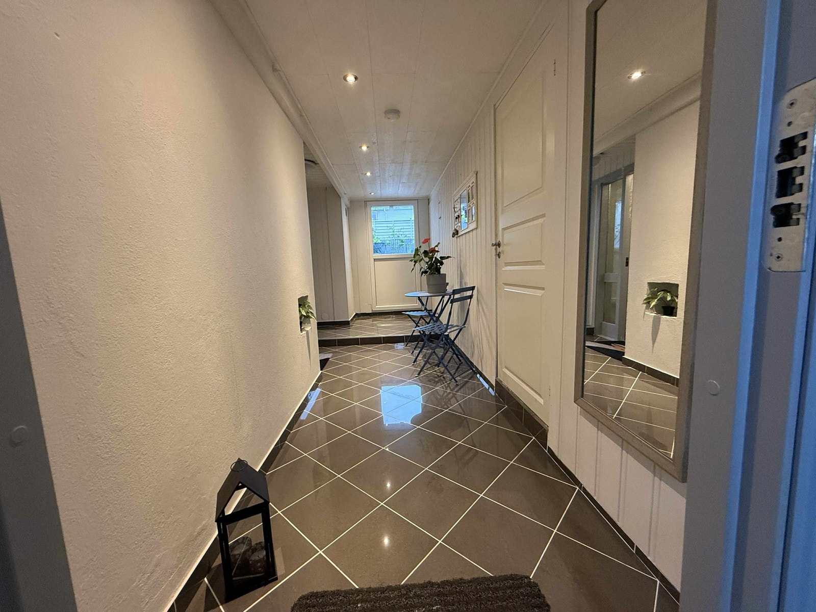Fra inngangsdøren møtes du av en lys og innbydende gang med flislagt gulv – en praktisk løsning som tåler både vær og vind. De hvitmalte panelveggene og downlights i taket gir et rent og moderne uttrykk. Galleribilde