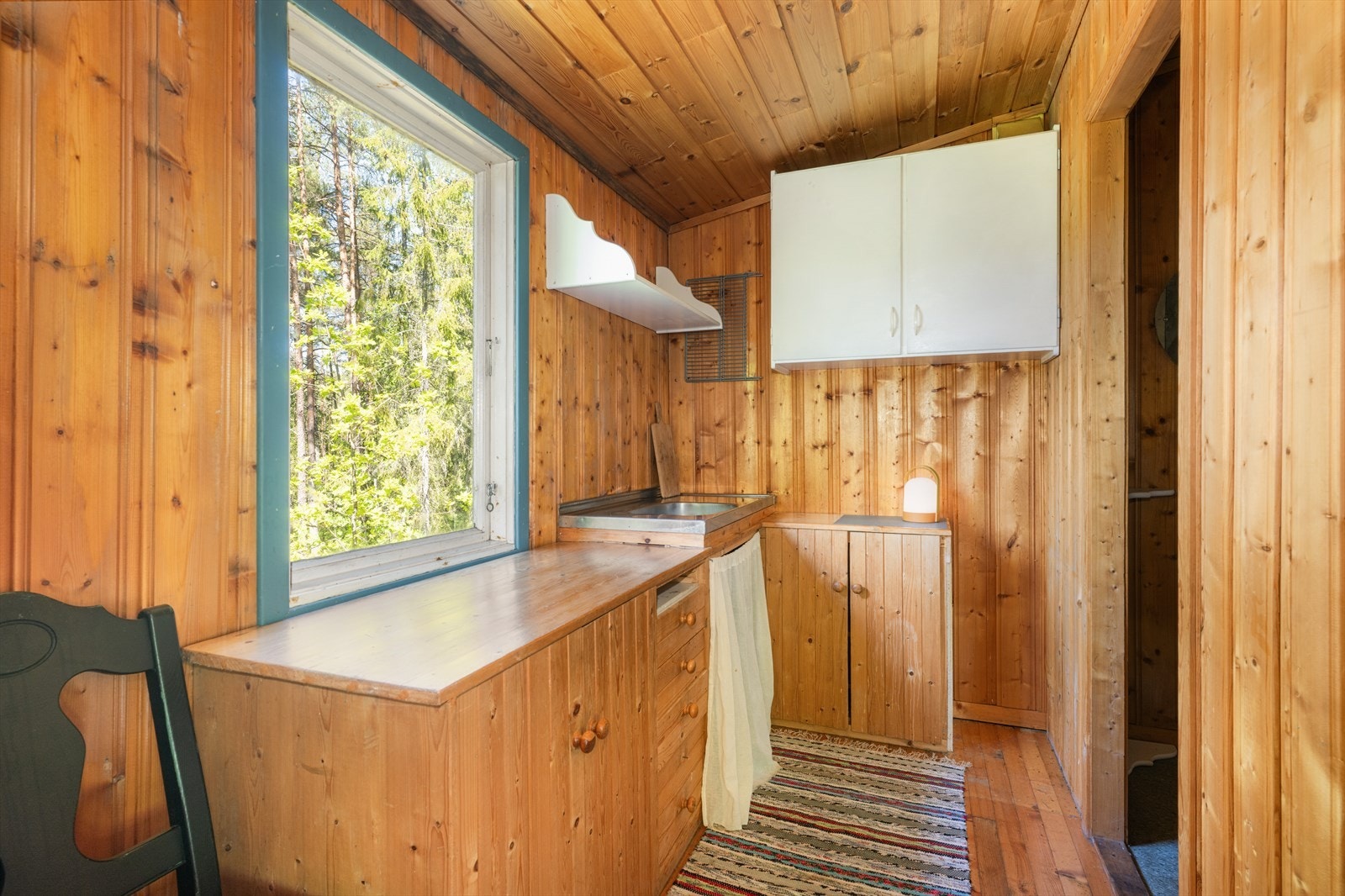 Videre er det åpen løsning til kjøkken fra stuen. Kjøkkenet har en eldre innredning og benkebeslag med stålkum med avløp ut i terreng. Galleribilde