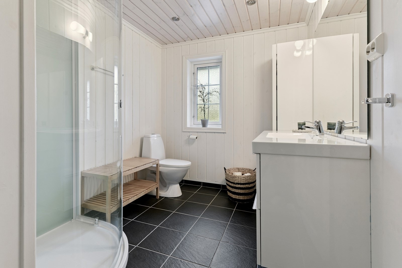 Bad med varmekablar på flislagt golv. På veggar er det lyst panel. Av innreiing har du dusjkabinett, golvståande toalett, høgskap og skuffeinnreiing med heilstøypt servant. Galleribilde