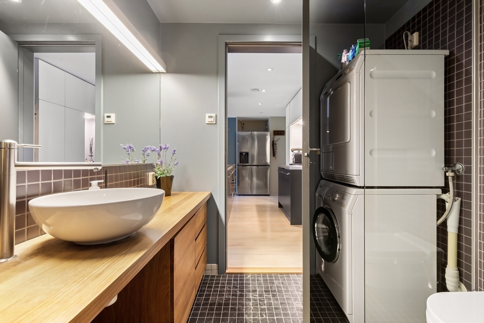 Baderomsinnredning bestående av benkeskap med glatte fronter, stort speil og belysning over servant - Opplegg for for vaskemaskin Galleribilde