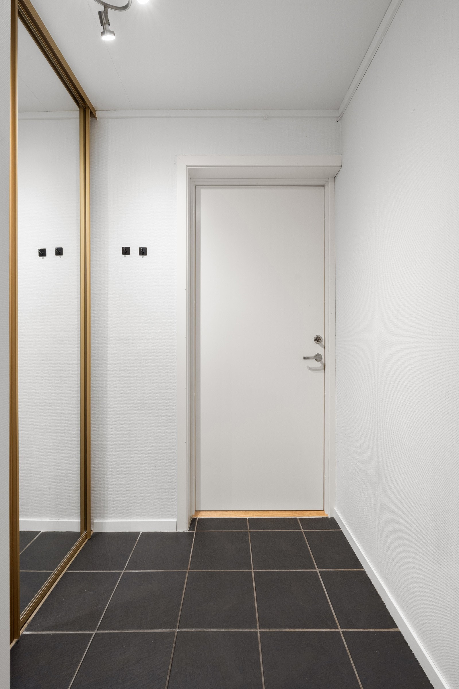 Flislagt gang med stor skyvedørsgarderobe.