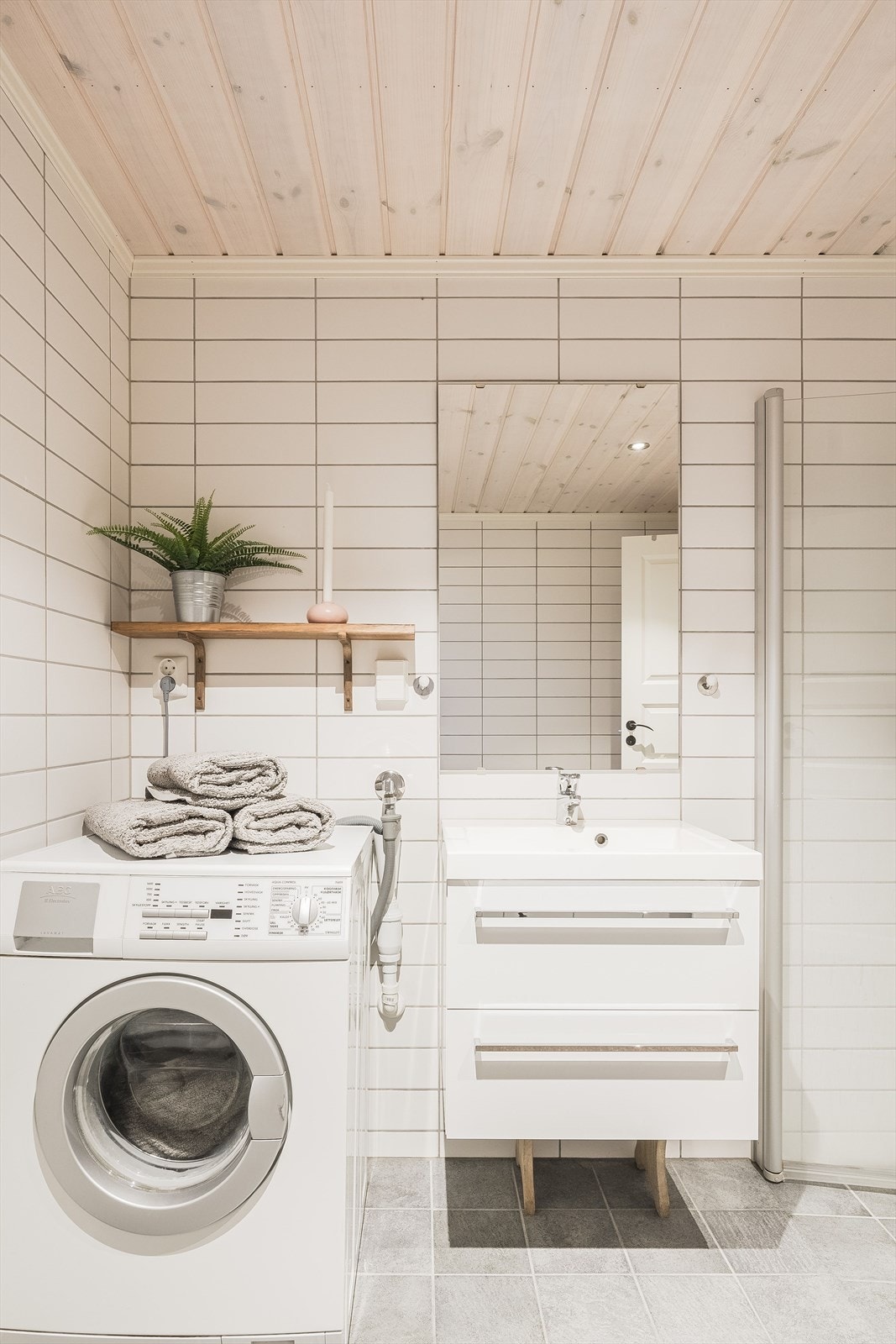 Moderne baderomsinnredning med skuffer og heldekkende servant, speil og vegghengt hylle med plass og opplegg for vaskemaskin under. Galleribilde