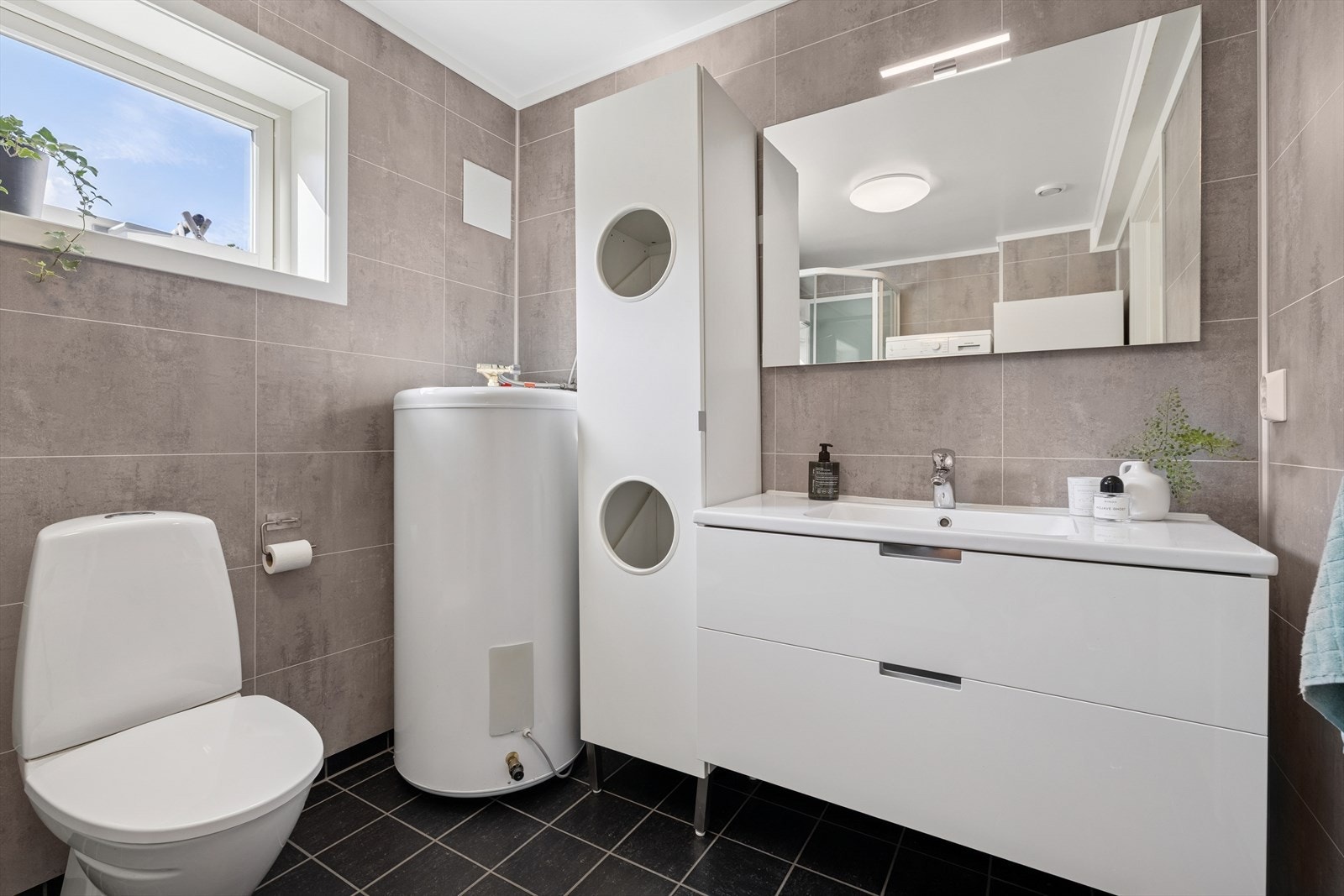 Bad/vaskerom beliggende i kjelleretasjen fra 2017 har fliser på gulv med gulvvarme, veggene har baderomsplater og taket er malt. Galleribilde