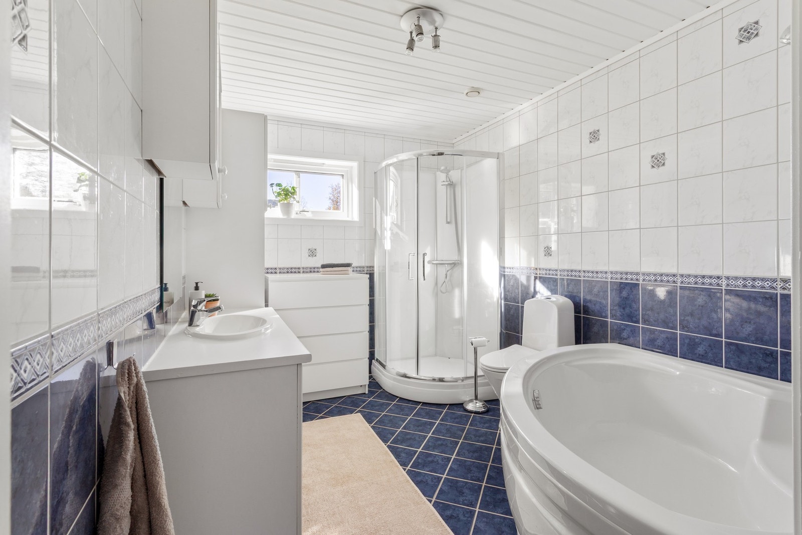 Flisbelagt baderom med innredning av badekar, dusjkabinett og gulv montert toalett Galleribilde