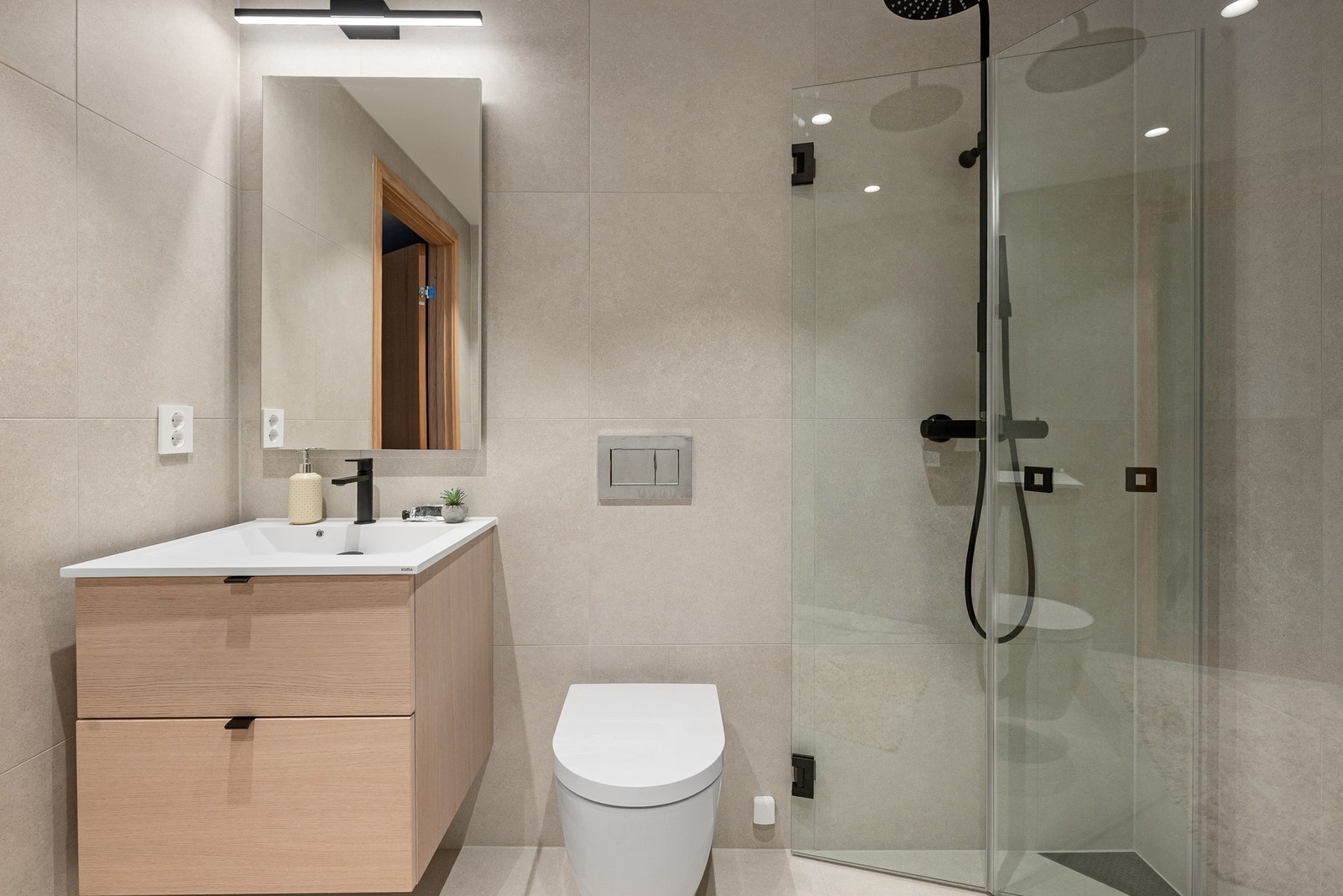 Badet har dusjhjørne med innfellbare dører, nisje med opplegg for vaskemaskin/tørketrommel, vegghengt wc, servantmøbel med skuffer og veggspeil. Galleribilde