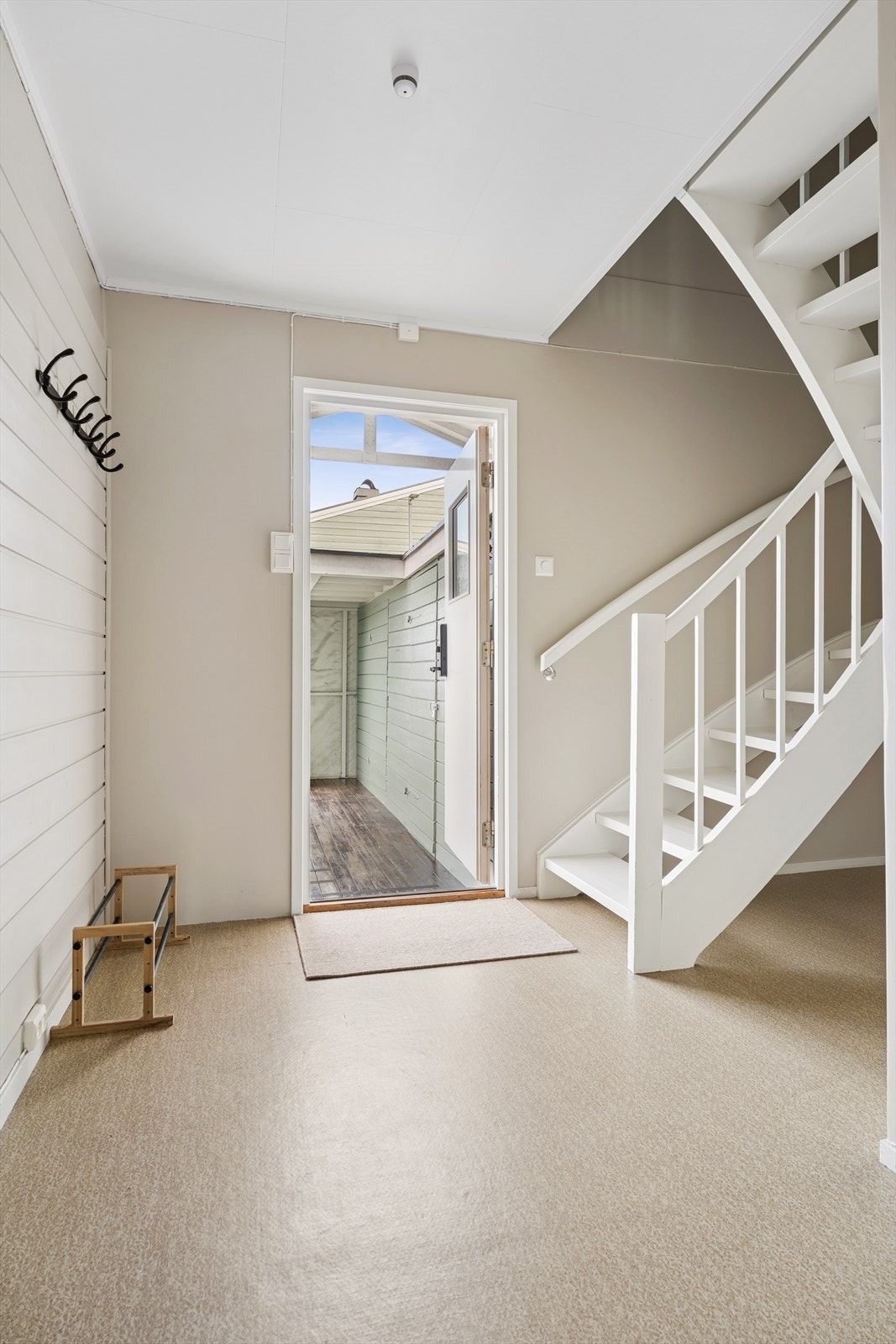Velkommen inn i en lys entré med trapp i treverk som leder opp til andre etasje. Galleribilde