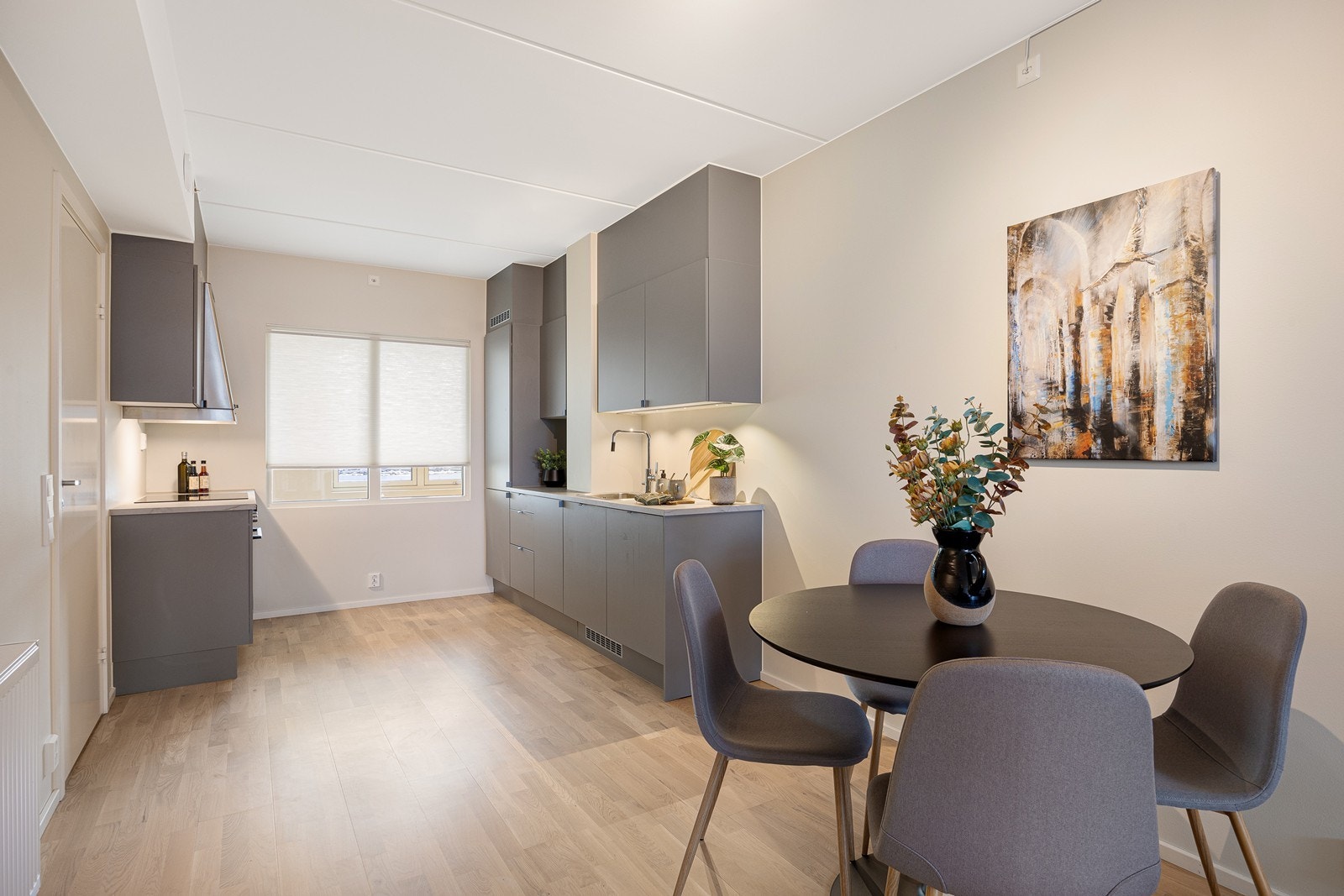 Kjøkkenet er stilrent, med grå, glatte fronter, takhøye skap og en lys benkeplate i marmorert laminat med nedfelt vaskekum i stål. Galleribilde