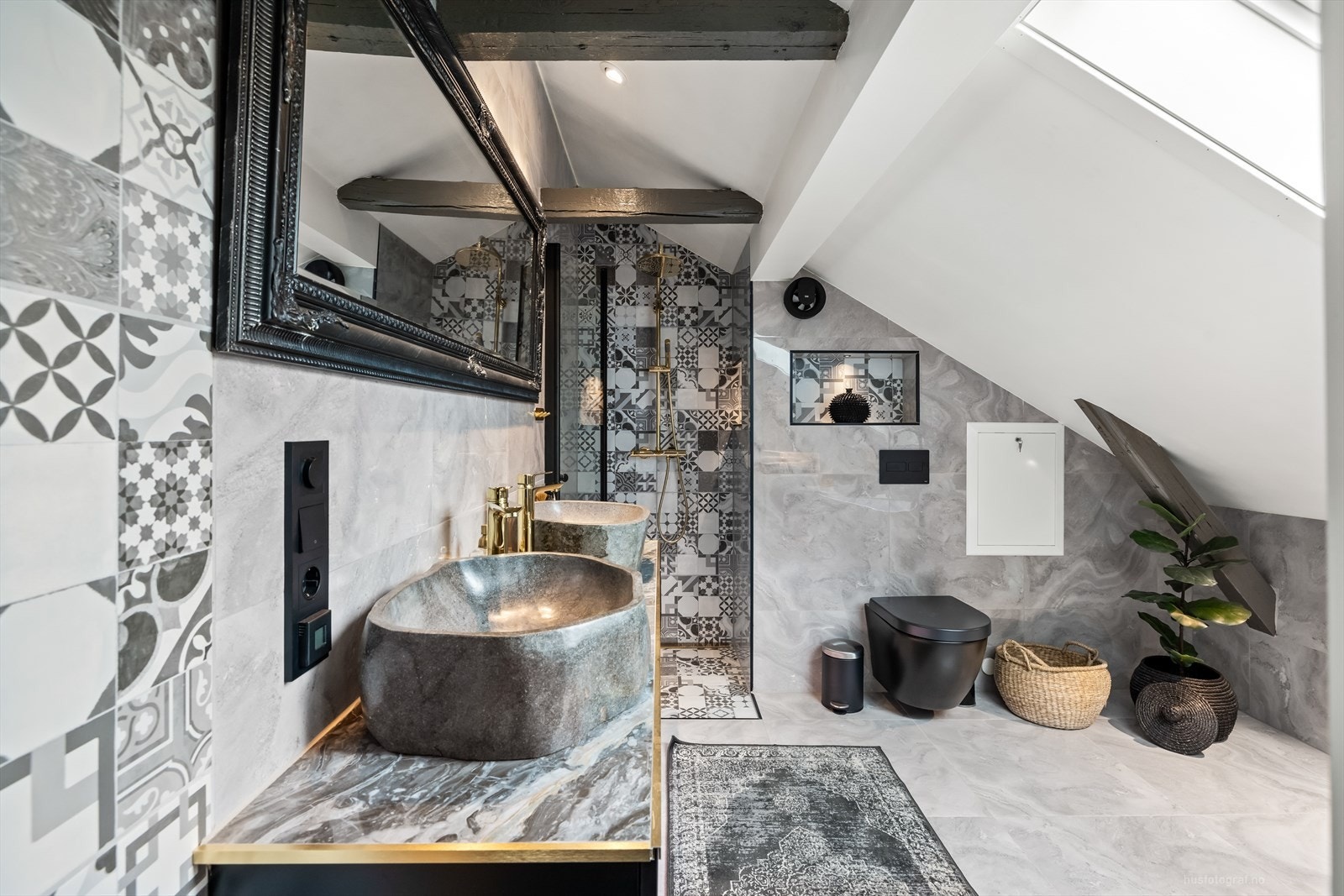 Den sorte baderomsinnredningen med glatte fronter. På benken troner to massive, håndhugde servanter i naturstein, supplert med stilrene armaturer i gull - et eksklusivt blikkfang. Galleribilde