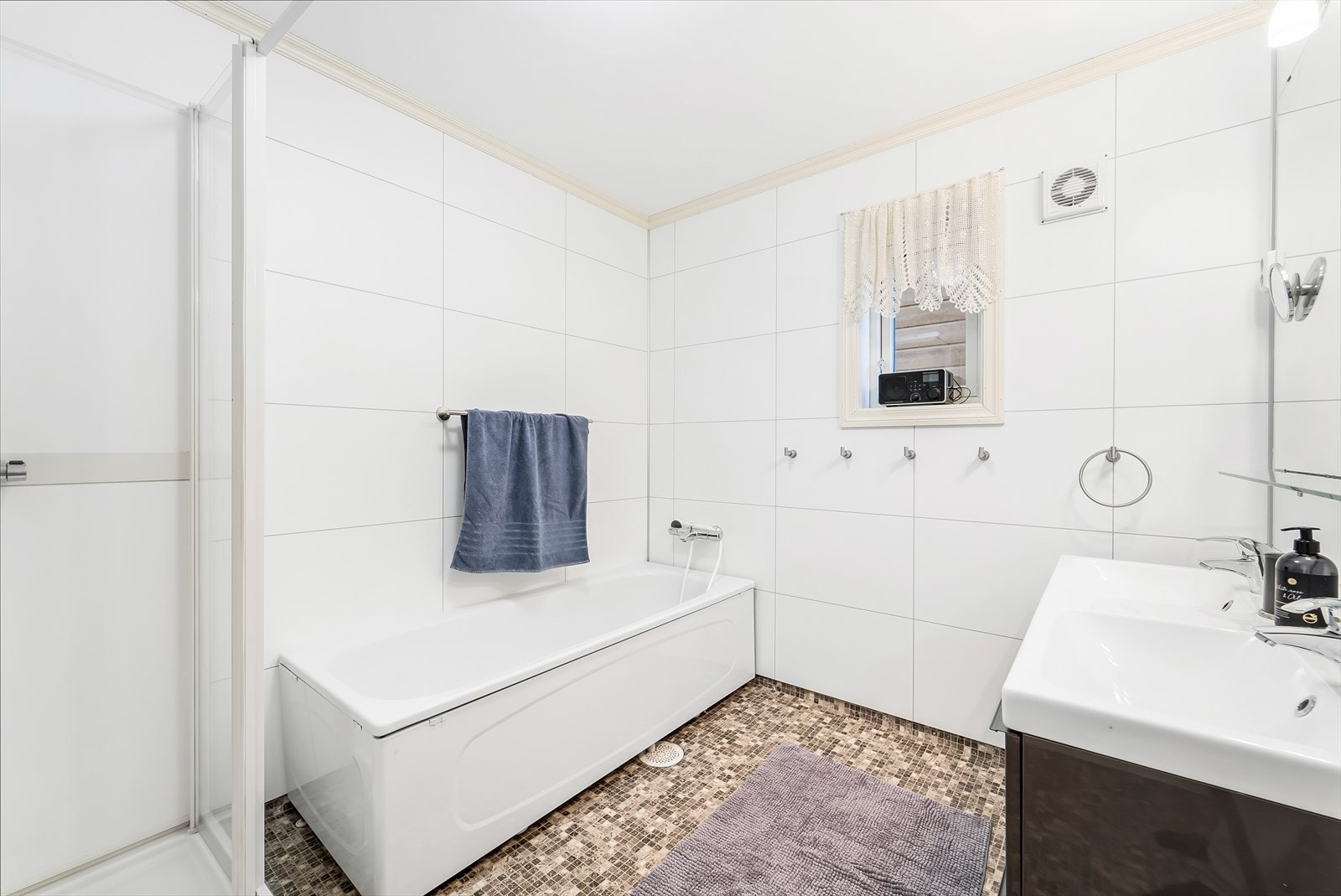 Tidløst innredet bad med belegg på gulv og baderomsplater på vegg. Innredet med baderomsinnredning, toalett og dusjkabinett. Galleribilde