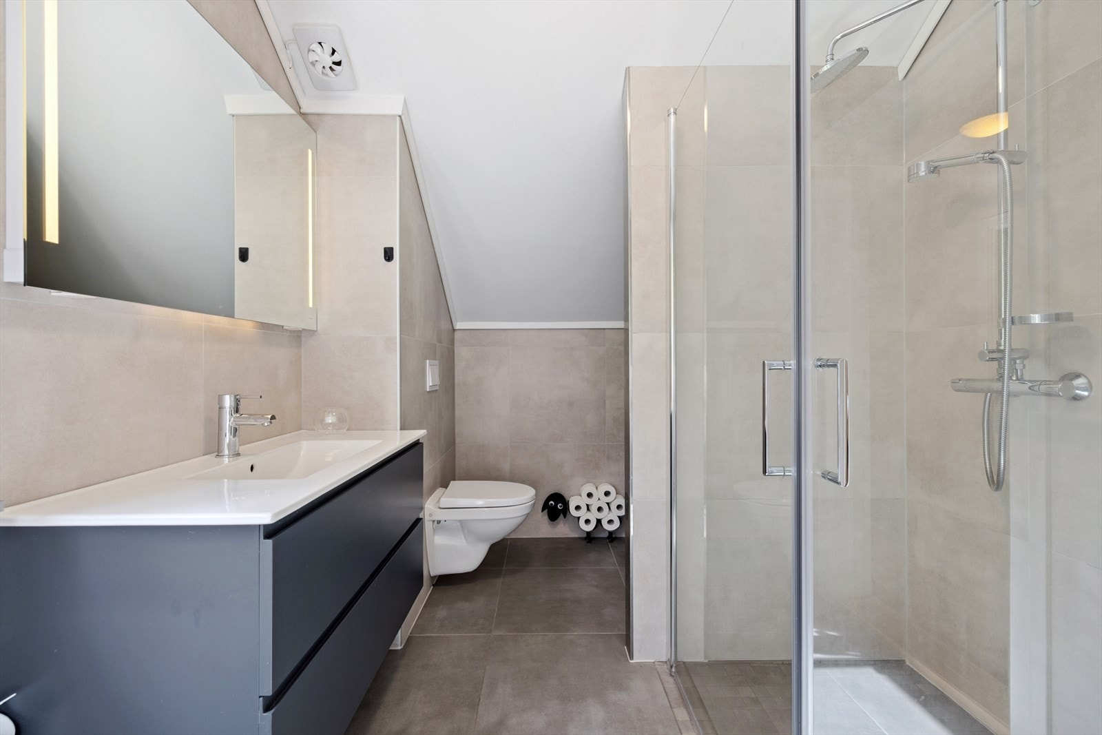 Rommet har innredning med nedfelt servant, veggmontert toalett, dusjvegger/hjørne og opplegg for vaskemaskin. Elektriske varmekabler Galleribilde