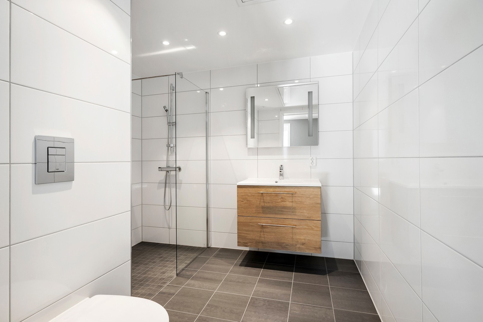 Baderom med moderne standard. Flislagt gulv i antrasitt med mosaikk i dusjsonen og hvite, blanke veggfliser. LED-spotter i himling med dimmer og gulvvarme gir både komfort og stil. Galleribilde