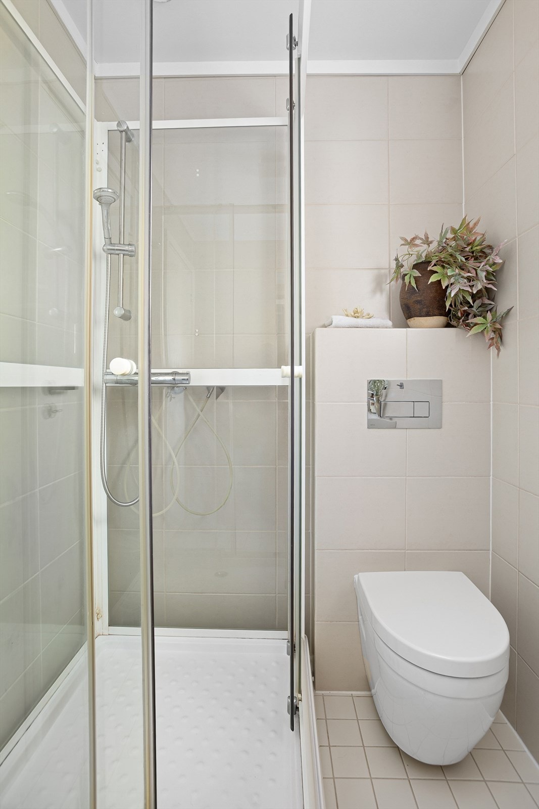 Baderommet er utstyrt med dusjkabinett, veggfestet klosett, servant, benkeskap med glatte fronter og speil over servant Galleribilde