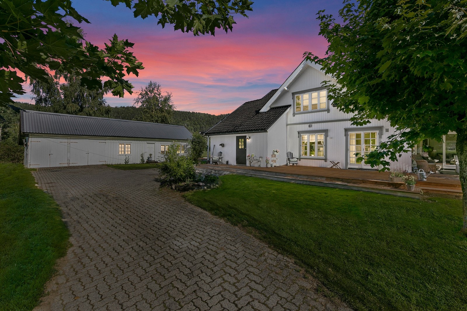 Innbydende gårdsplass pent opparbeidet med belegningsstein, prydbusker og trær. Galleribilde