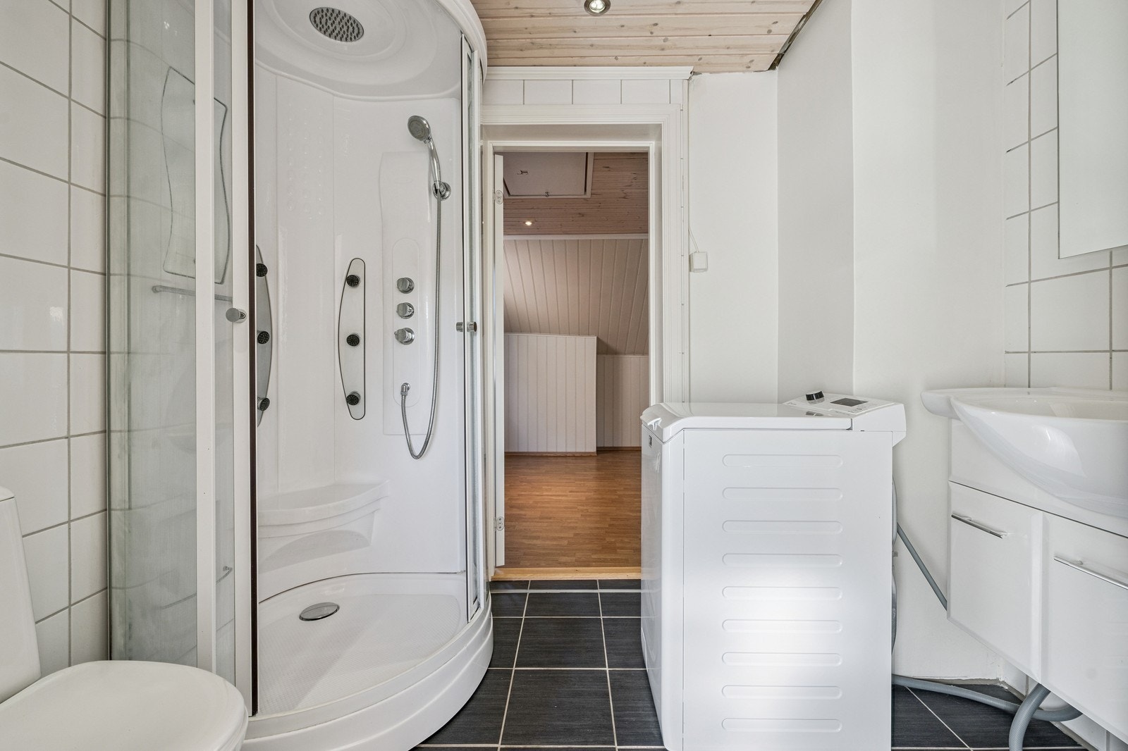 Flislagt bad med dusjkabinett, toalett, servant og toppmatet vaskemaskin Galleribilde