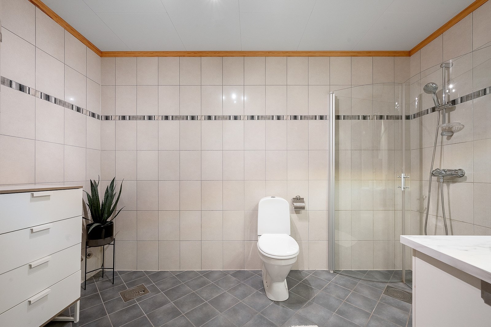 Badet har fliser på gulv med varmekabler, fliser på vegg, og malte takplater. Galleribilde