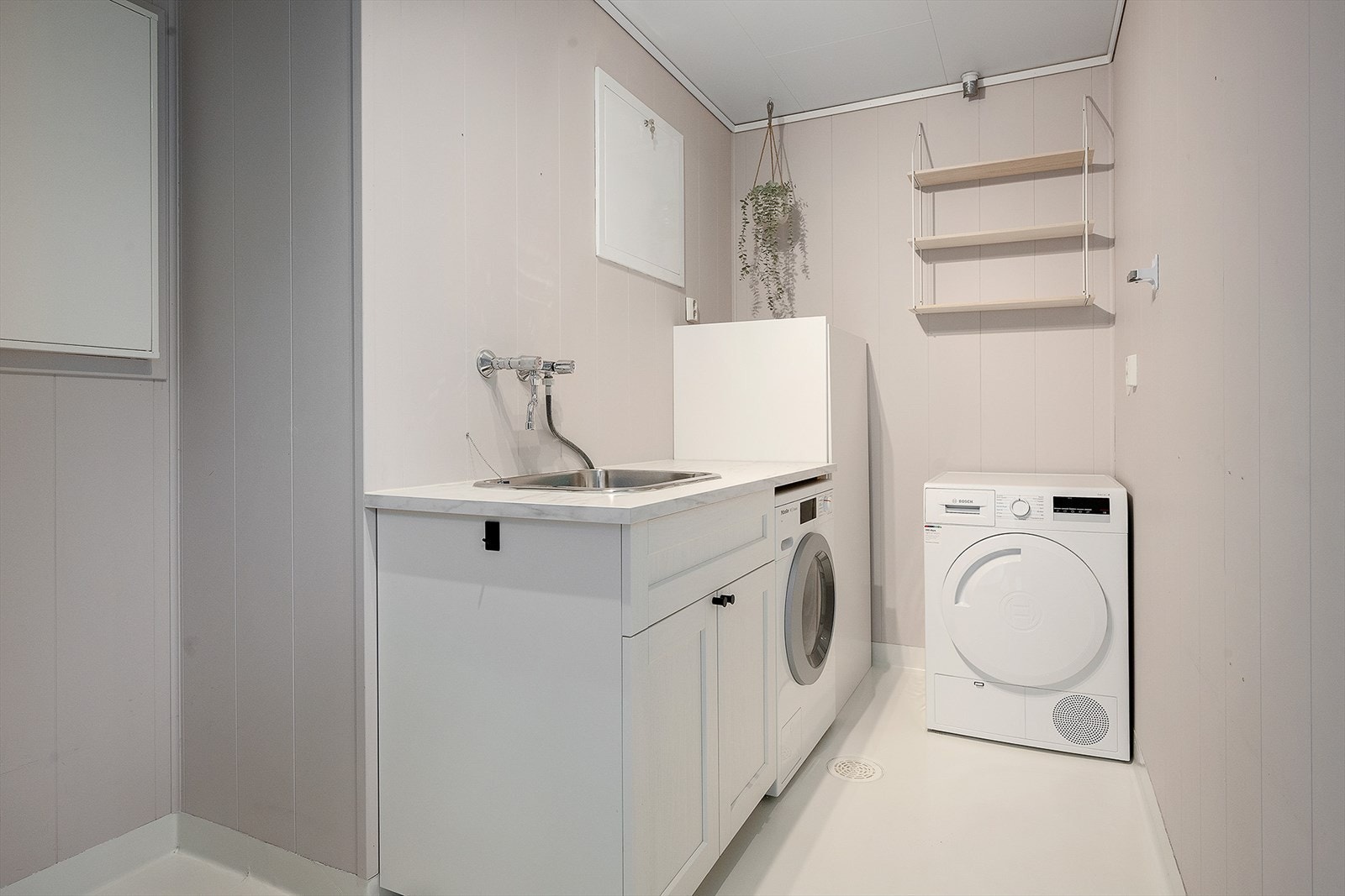 Vaskerommet har belegg på gulv, finérplater på veggene og takplater i tak. Her er det innredet med underskap, benkeplate og nedfelt skyllekar, samt opplegg for vaskemaskin. Galleribilde