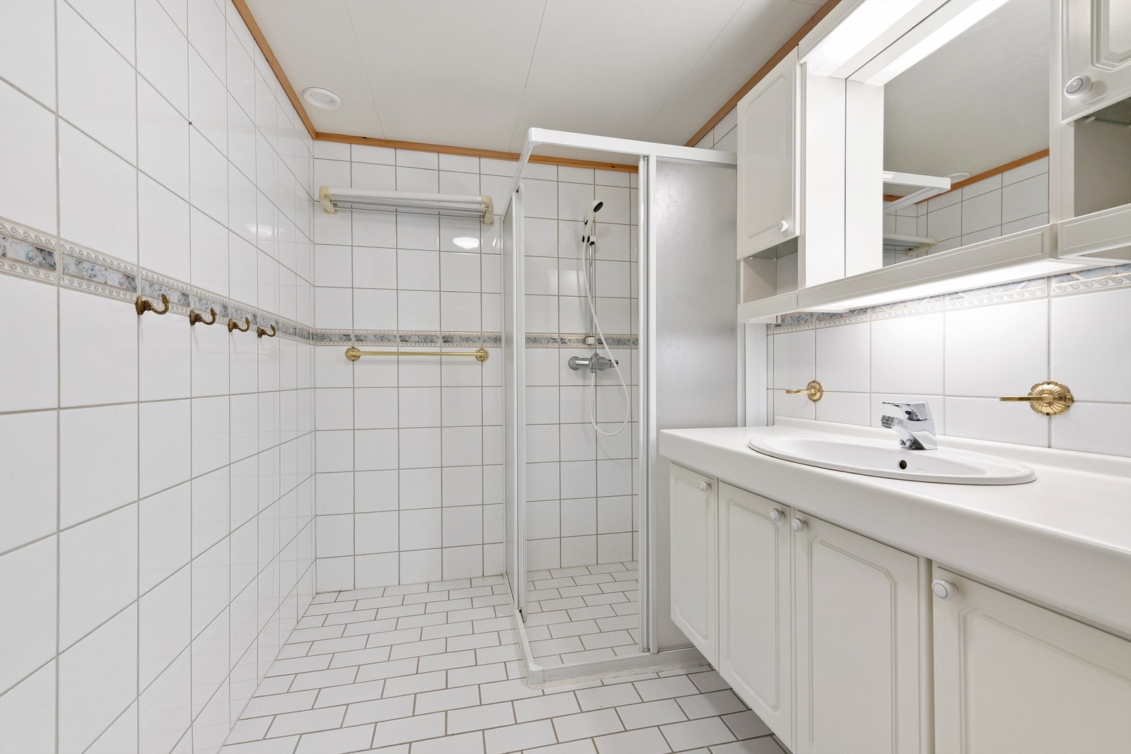 Flislagt bad med romslig innredning. Dusjhjørne med dører og vegghengt dusjarmatur Galleribilde