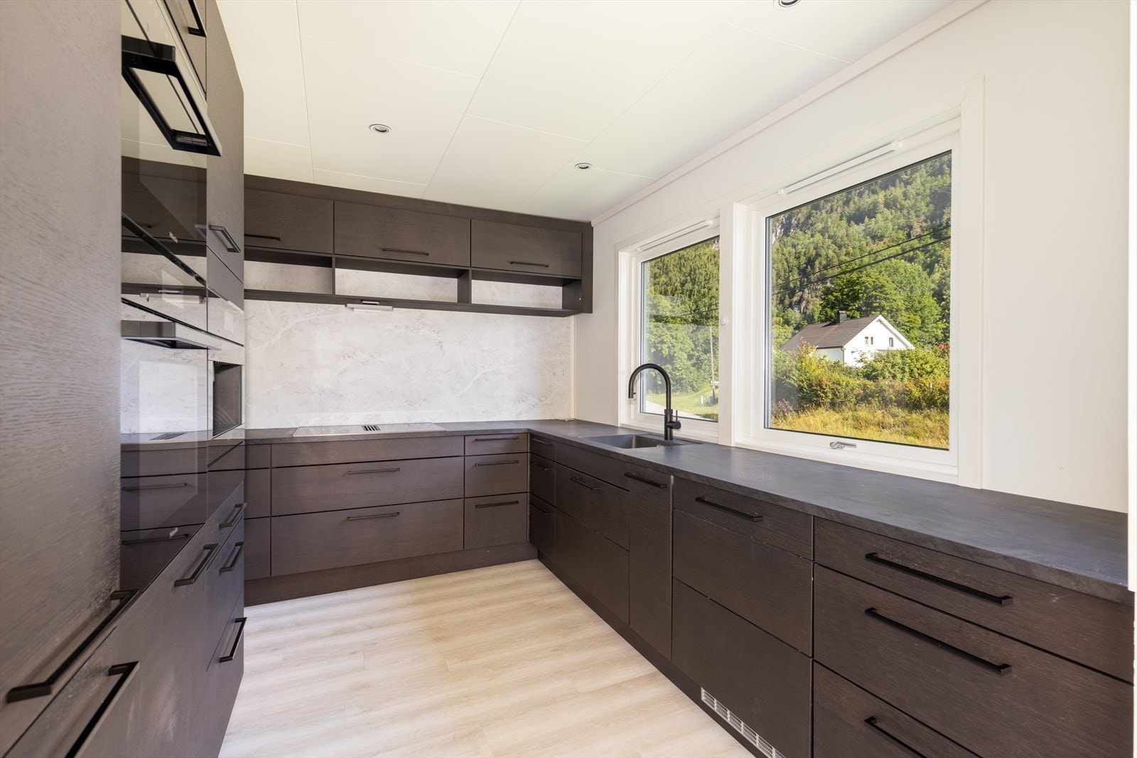 Kjøkkenet har et hypermoderne uttrykk, i mørk utførelse med hel seksjon med høyskap. Store vindusflater tilfører godt med arbeidslys inn på kjøkkenet, hvor det er gode arbeidsflater på laminerte benkeplater. Galleribilde