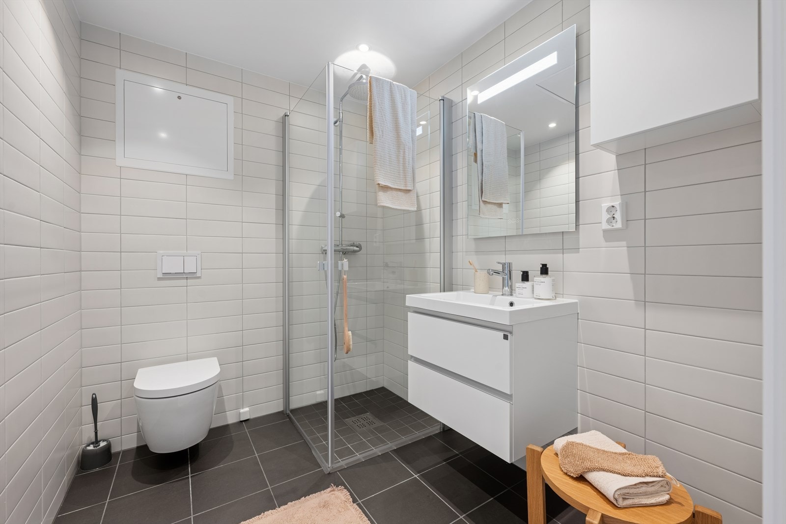 Badet er lekkert og lyst med mørke fliser på gulvet og lysere fliser på veggene - tidløst og elegant Galleribilde