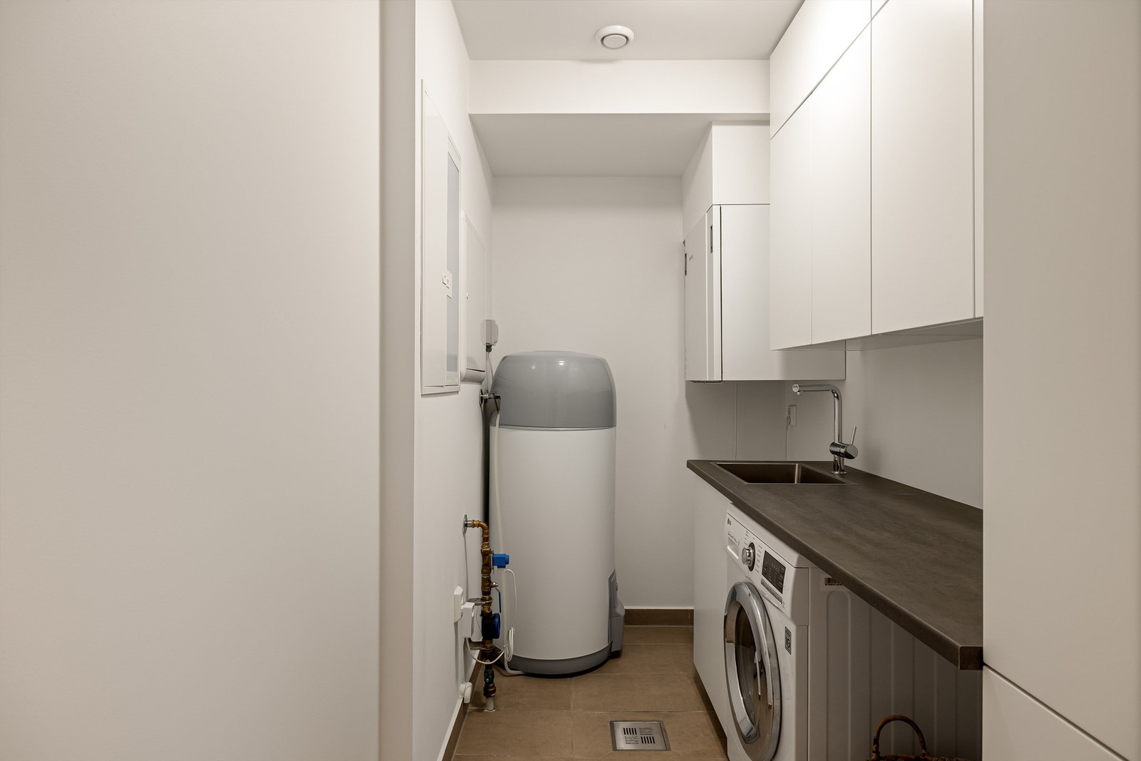 Teknisk rom har opplegg for vaskemaskin, oppbevaringsskap og praktisk arbeidsbenk. Galleribilde