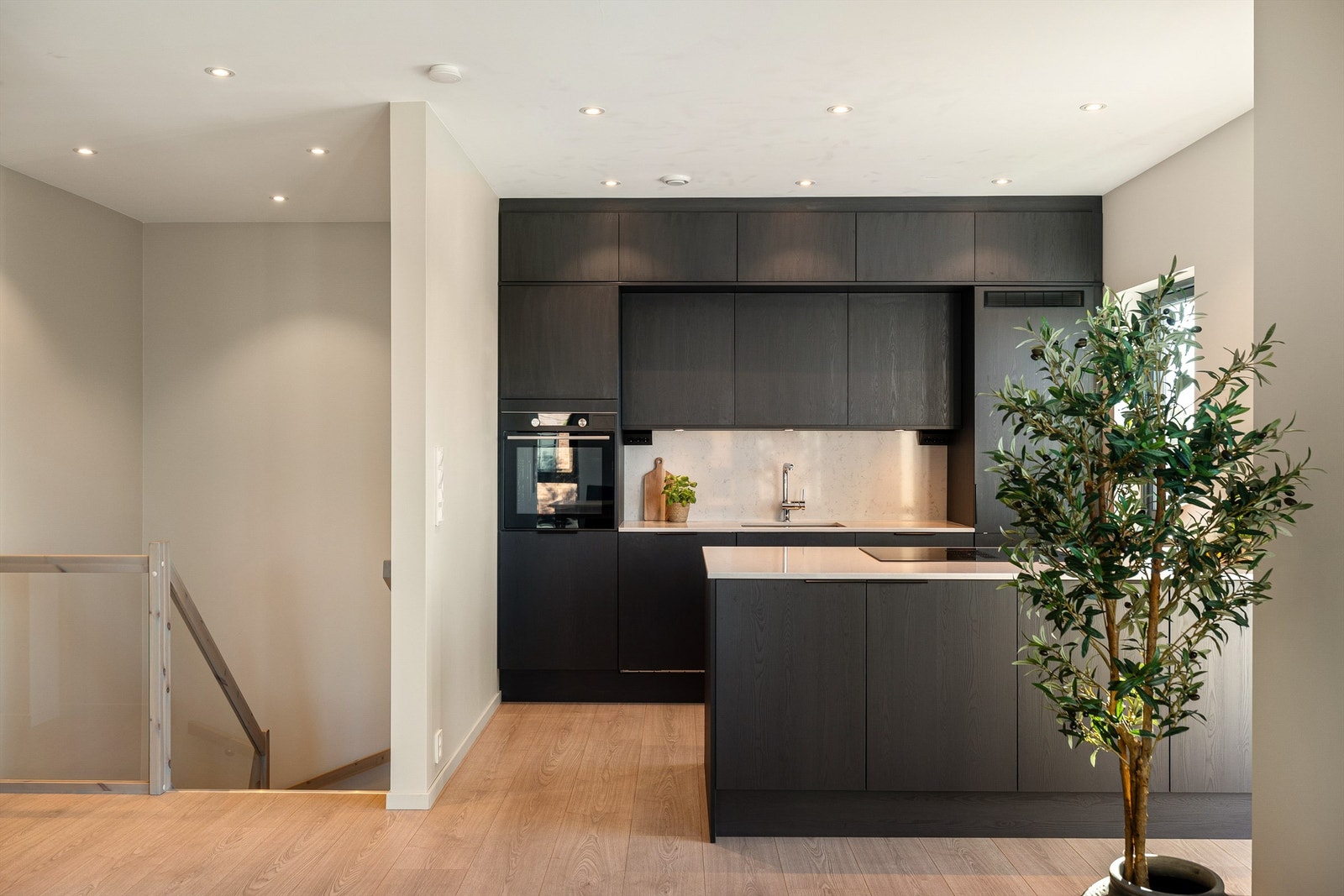 Kjøkken med mørke fronter, og flott øy med platetopp og oppbevaring i skaper. Galleribilde