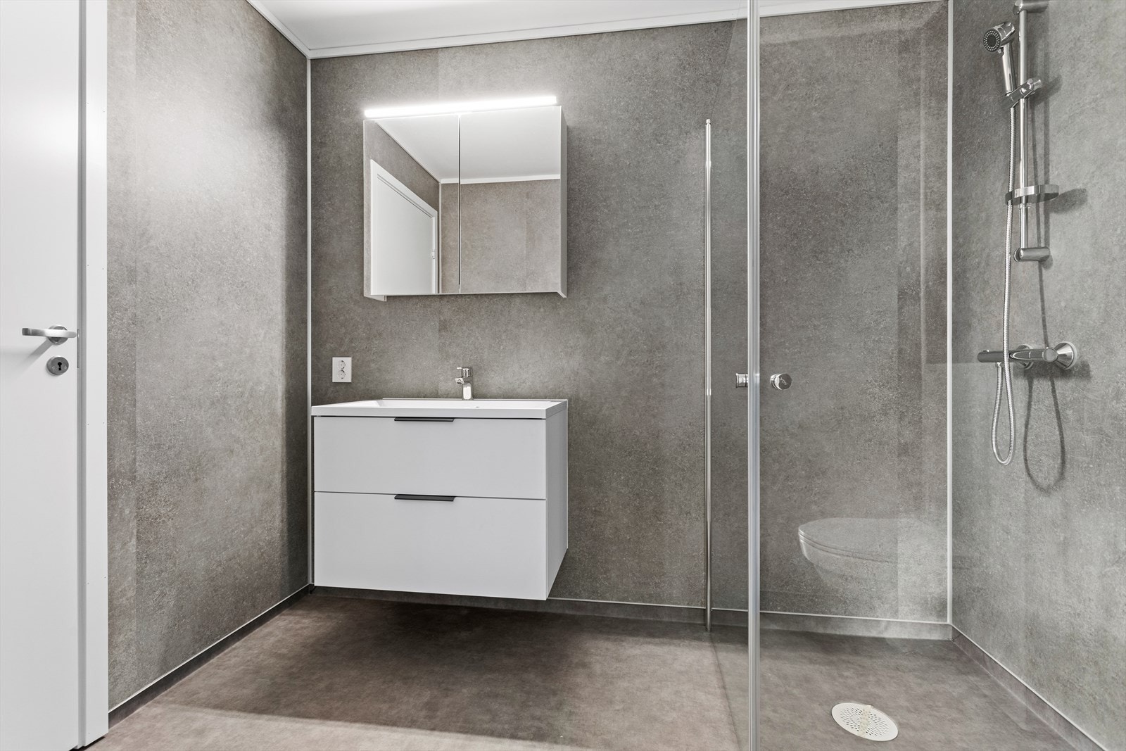 Vidare er badet utstyrt med baderomsmøbel, speilskap, dusjhjørne og vegghengt toalett. Galleribilde