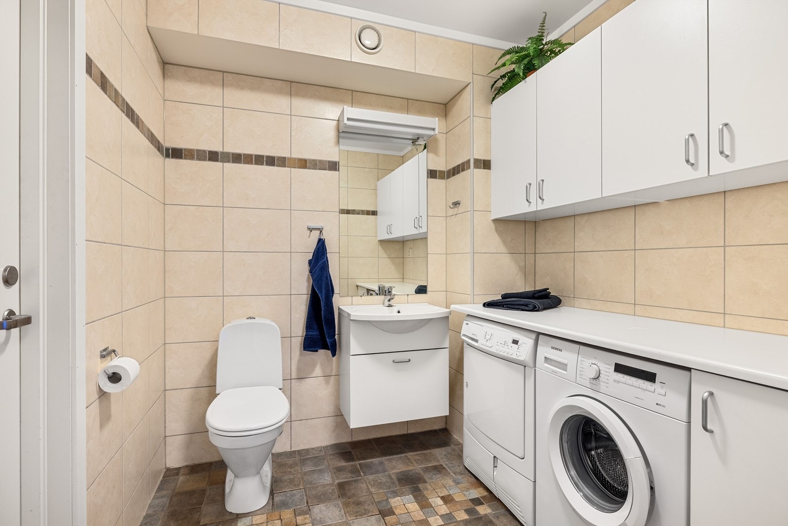I tillegg til badet er det er meget praktisk, flislagt vaskerom med godt med skapplass og plass og opplegg for både vaskemaskin og tørketrommel under benkeplate. I tillegg er det toalett og servantskap med speil og lys i overkant. Galleribilde