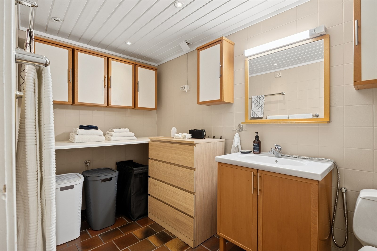 Baderomsinnredningen består av et frittstående wc, servant med underskap, spel med overlys, veggskap, benk og hjørnedusj med inn-/utadslående dusjdører. Galleribilde