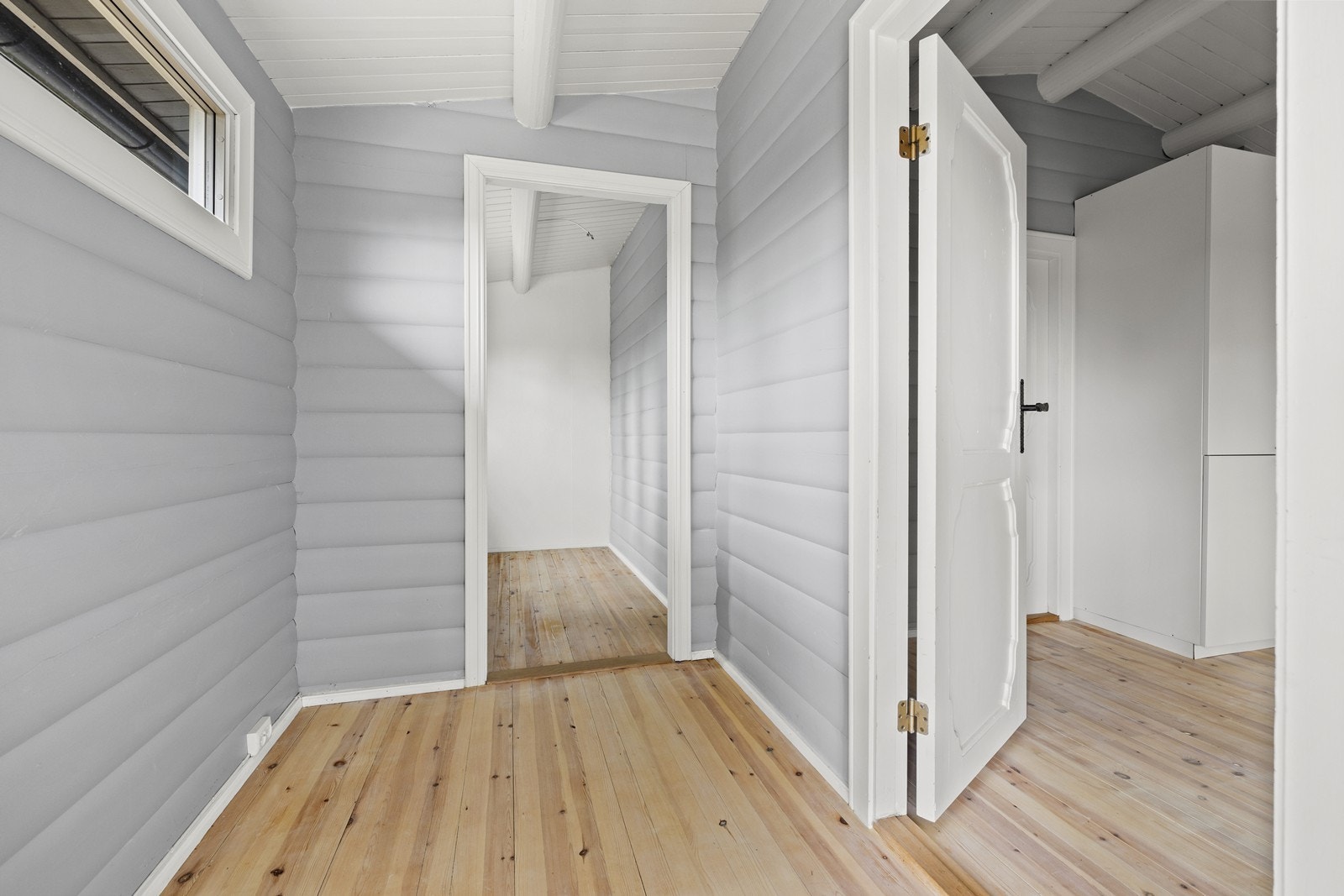 Lys og romslig entré med furugulv og panel på vegger og himling. Galleribilde