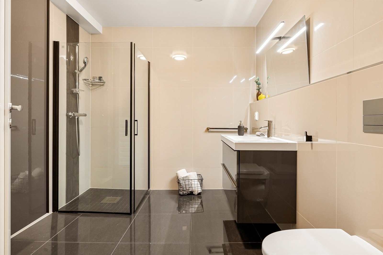 Helfliset bad med lyse fliser på vegg og mørke fliser på gulv. Badet ligger i hoveddelens 1. etasje og har varme i gulv. Galleribilde