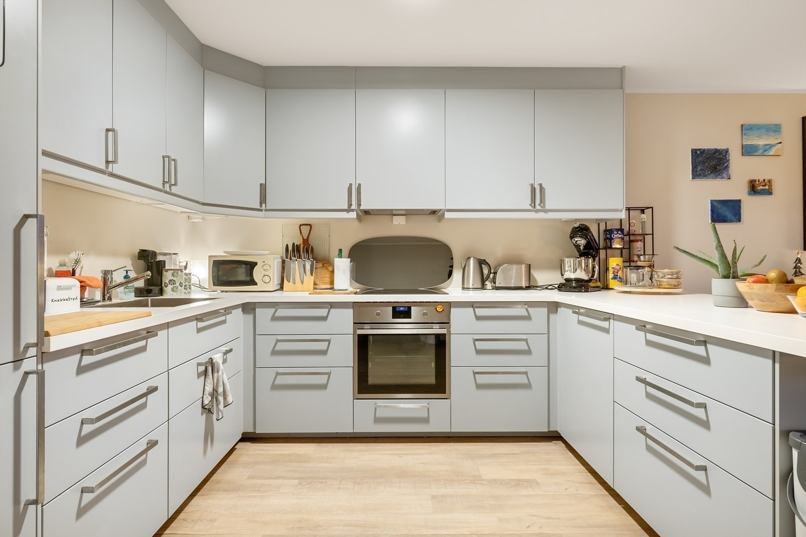 Kjøkkenet i leiligheten har stilrene fronter i behagelig blåtone med laminat benkeplate. Her er det integrert stekeovn, platetopp, oppvaskmaskin, og kjøleskap med frys. Galleribilde