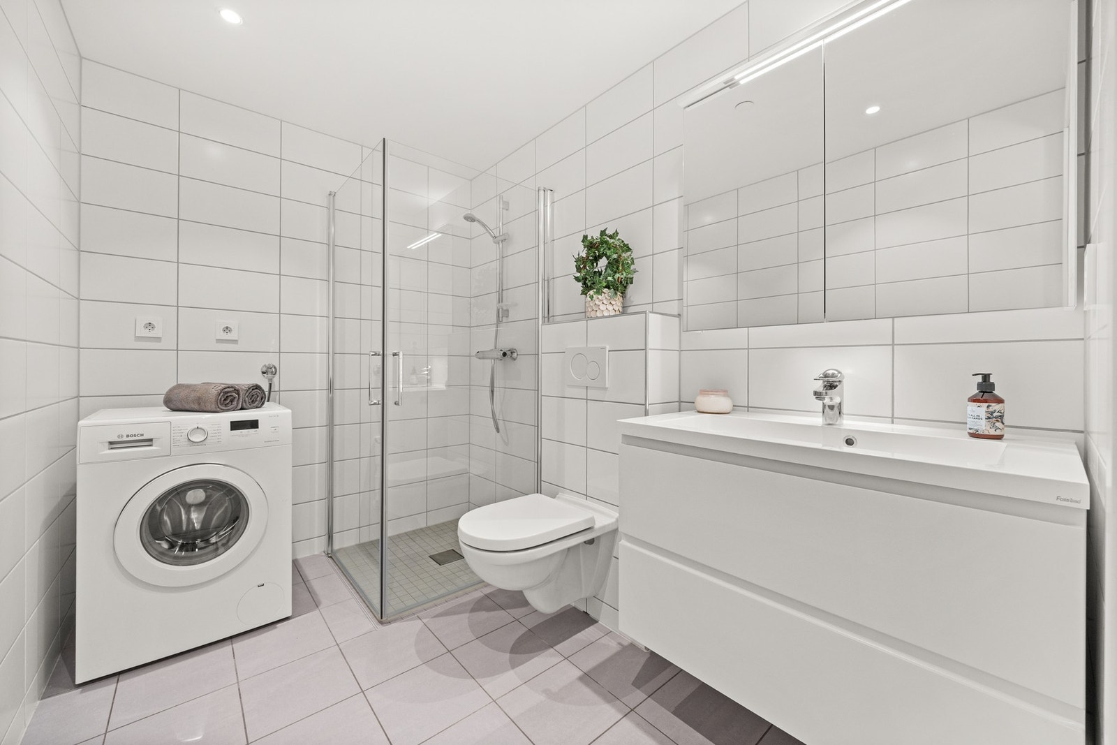 Badet har flislagte vegger, gulv med gulvvarme og opplegg for vaskemaskin Galleribilde