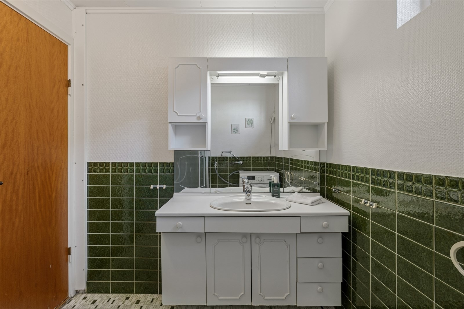 Eldre baderom med fliser på deler av veggen og mosaikkfliser på gulvet. Galleribilde