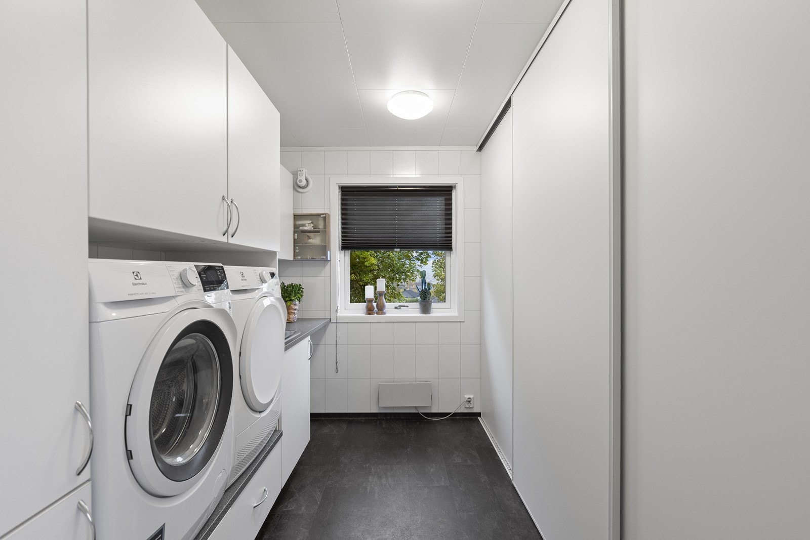 Vaskerom med praktisk skyvedørsgarderobe og innredning med skap, benk og skyllekar. Galleribilde