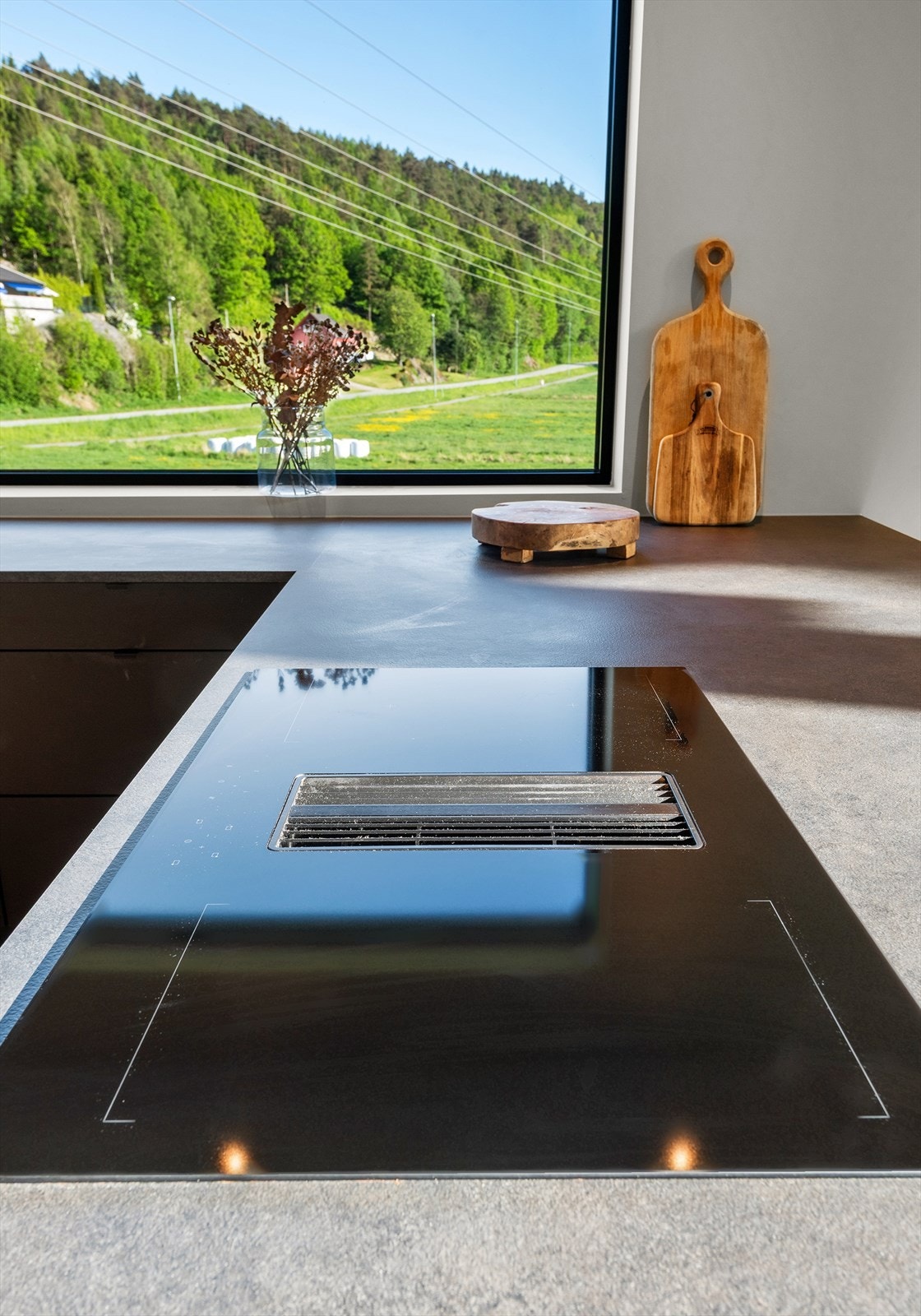 Lyst kjøkken med moderne platetopp. Store vinduer gir flott utsikt til frodig natur, og inviterer lyset inn i rommet..jpg Galleribilde