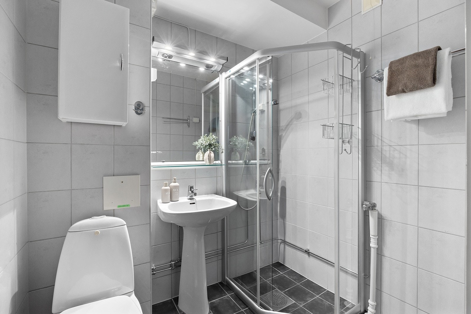 Innredning på bad fremstår med dusjhjørne, søyleservant, speil med lys over, overskap, opplegg for vaskemaskin og wc. Galleribilde