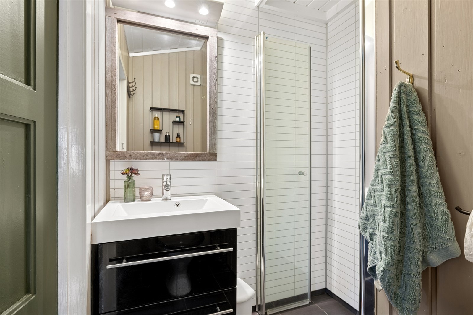 Badet har fliser på gulvet, sokkelflis langs veggene og våtromsplater i dusjnisjen. Øvrige vegger og himling har panel som gir et lunt og tradisjonelt uttrykk. Rommet er innredet med servant, toalett og dusj. Galleribilde