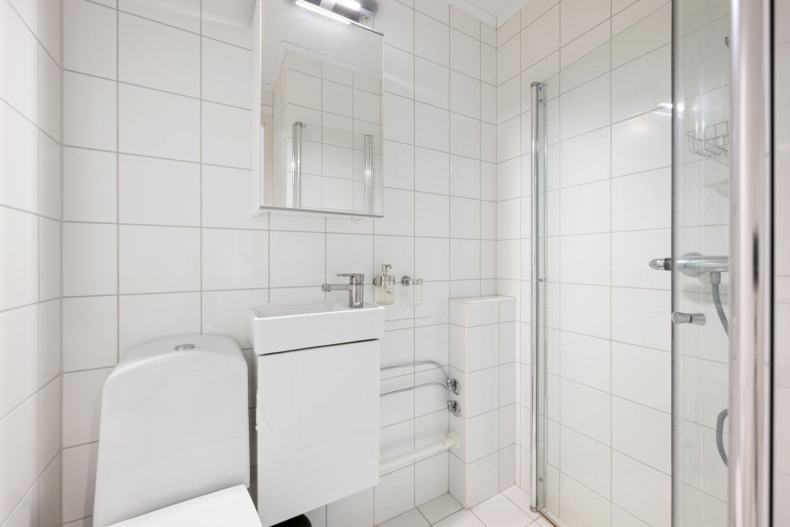 I boligens tredje etasje ligger også et baderom som er helfliset med hvite fliser og innredet med dusjhjørne, toalett, servant med skap under og tilhørende speilskap. Galleribilde