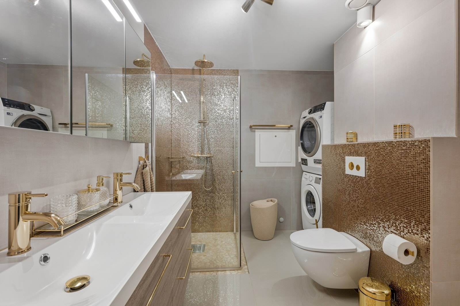 Badet ble pusset opp i 2018 og er tidløst innredet med en kombinasjon av grå og gull fliser. Badet er ellers utstyrt med dusjhjørne, veggehengt toalett og dobbel servant med skuffer under, tilhørende veggskap og speilskap. Galleribilde