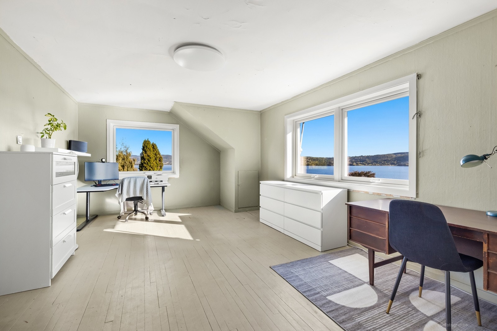 Oppe ligger en stor og romslig stue med fjordutsikt, peisovn og lyse overflater med malt tregulv. Galleribilde