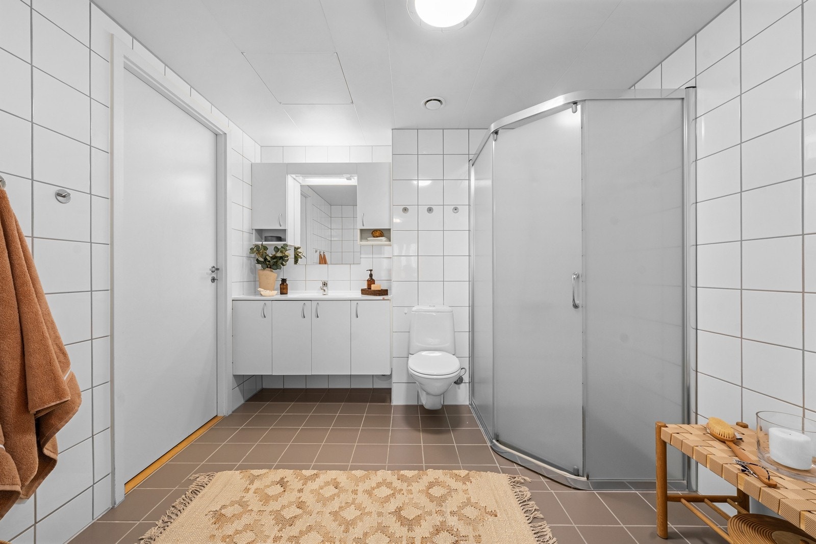 Badet har flislagt gulv med gulvvarme og flislagte vegger fra 2008. Himlingen består av takplater. Innredningen inkluderer vegghengt servantskap med dører, ovenpåliggende servant med ett-greps armatur, speil med overlys og dusjnisje med glassvegg. Galleribilde