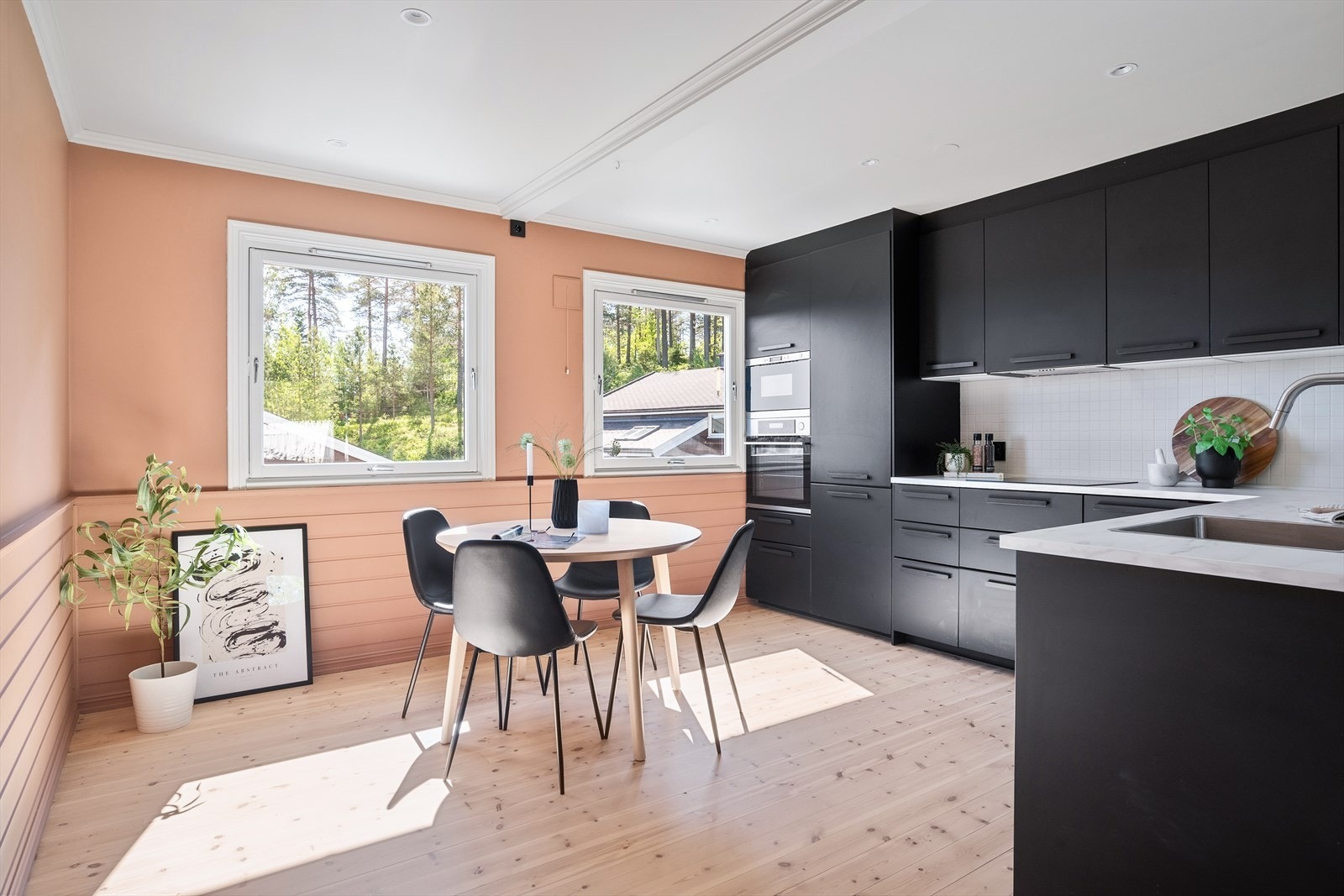 Innredning med moderne, sorte fronter og praktisk løsning med både over- og underskap. Hvite fliser mellom benkeplate og overskap, samt lys under overskap. Galleribilde