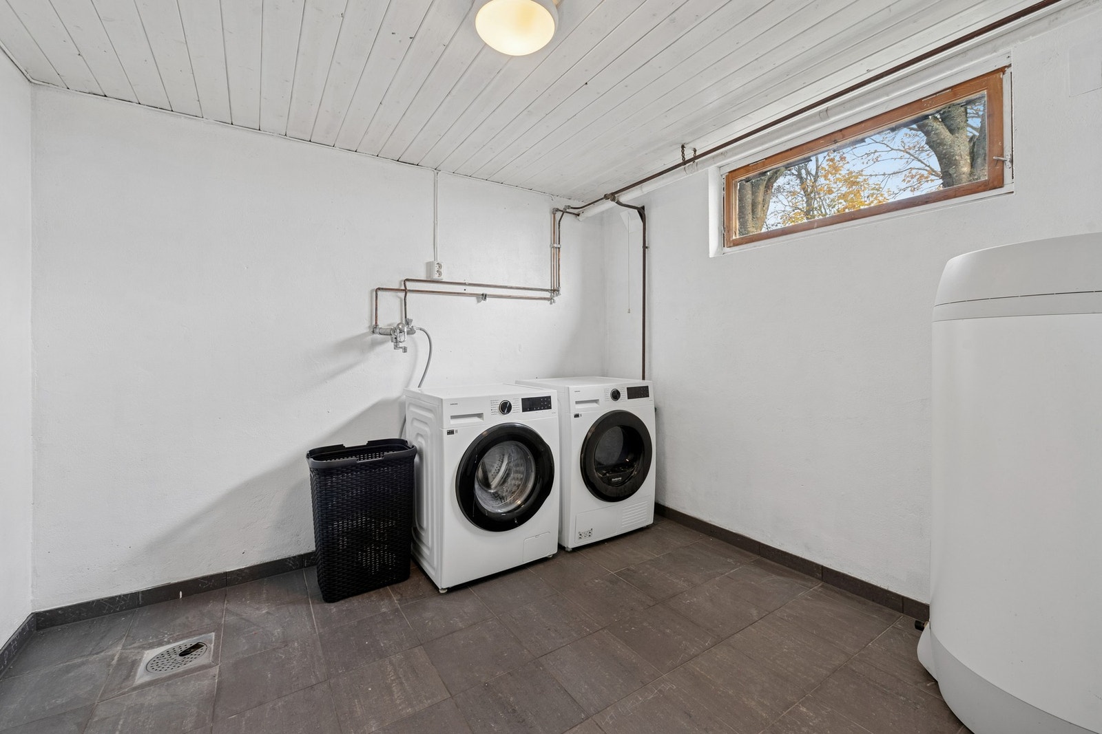 Praktisk vaskerom med flislagt gulv og malte overflater. Rommet har opplegg for vaskemaskin og tørketrommel, samt utslagsvask og varmtvannsbereder. Galleribilde