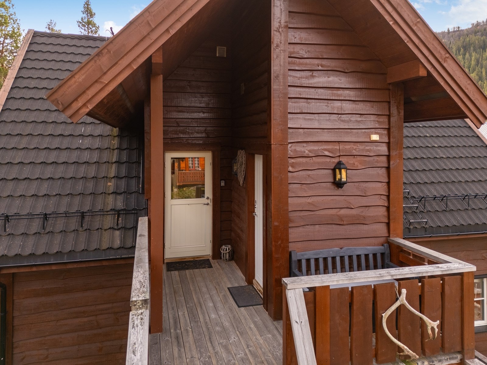 Delvis overbygget terrasse med sofa til å nyte kveldssola. Inngang til bod ved siden av inngangsdøra. Galleribilde