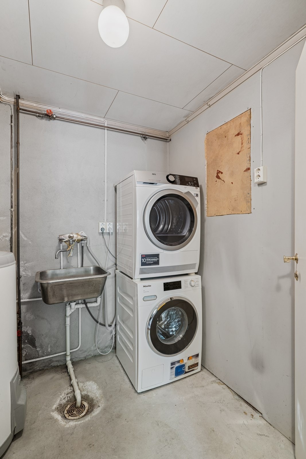 Vaskerommet i underetasjen har betong på vegger og gulv. Her er det innredet med utslagsvask, varmtvannsbereder og opplegg for vaskemaskin. Galleribilde